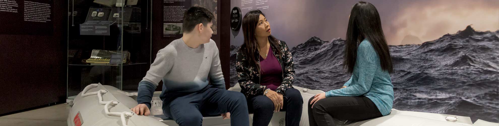 Trois personnes sont assises dans un canot de sauvetage et regardent un panneau d’exposition représentant des vagues dans l’eau.