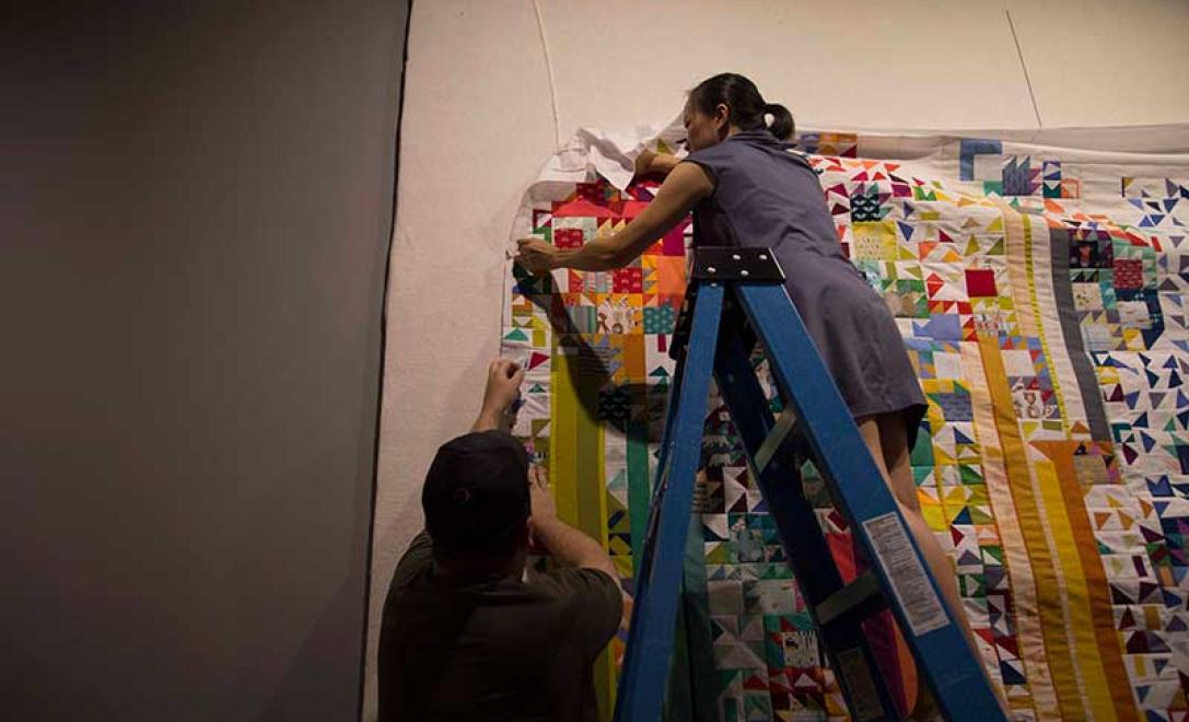 Une femme peut être vue essayant d’accrocher une couette au mur.