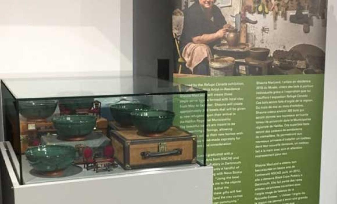 Vitrine vitrée avec bols de poterie à l’intérieur et une bannière se tient à côté avec une image de l’artiste qui a créé les bols.