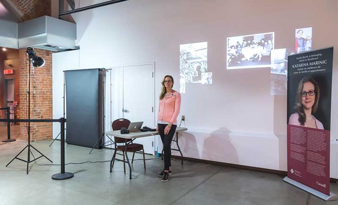 Une femme en chandail rose se tient à côté d’un bureau et des images sont projetées sur le mur derrière elle.