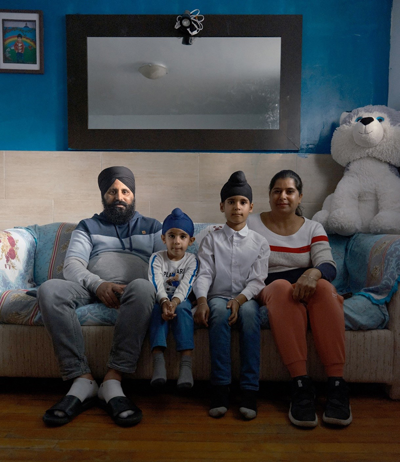 Une famille de quatre personnes est assise sur un canapé pour prendre leur photo; il y a un grand miroir sur le mur derrière eux.