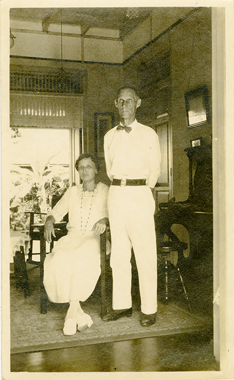 Une femme en blanc est assise, un grand homme en blanc se tient à côté d’elle.