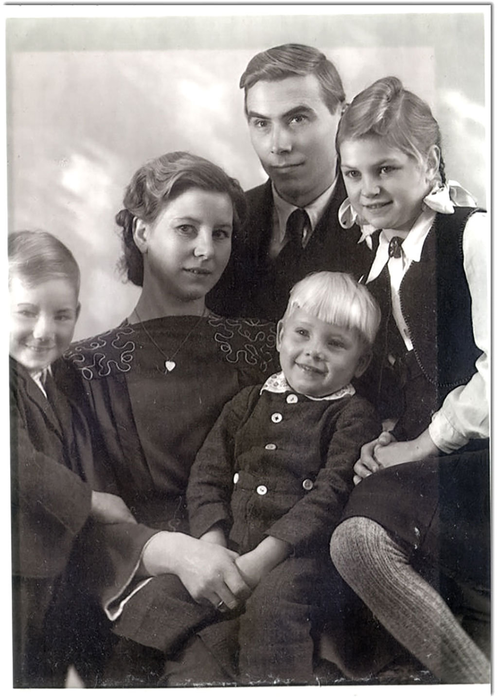 Une famille de cinq personnes. Ils sont assis ensemble, ont de doux sourires et portent des vêtements propres.