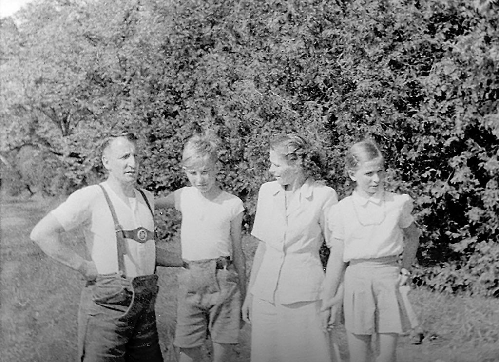 Une famille de quatre personnes debout, l’air reposé. Ils sont dans un parc et forment une rangée devant des arbres.