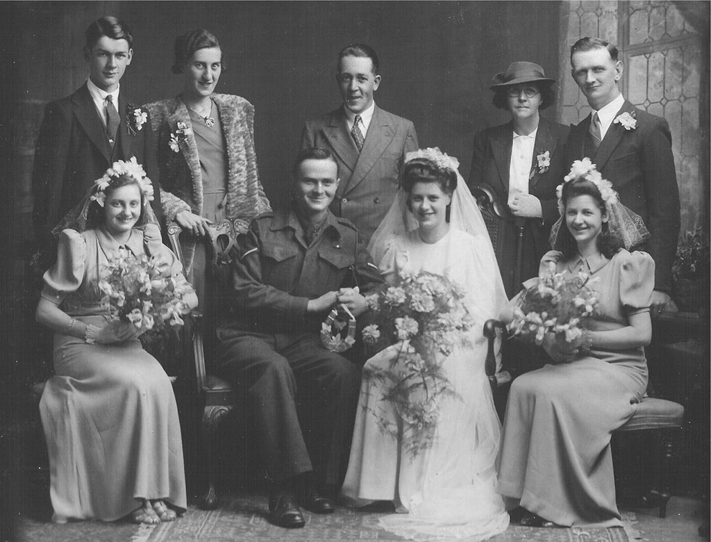 Portrait d’archive de trois mariées souriantes avec leurs bouquets; leurs époux sont debout derrière elles.