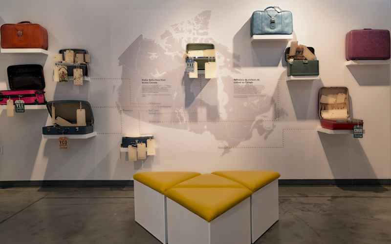 Dix bagages sont exposés sur un mur avec un texte et une carte du Canada.