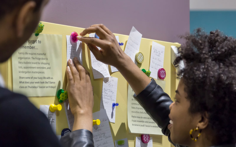 Deux personnes font une activité consistant à afficher des morceaux de papier avec de l’écriture sur un tableau.