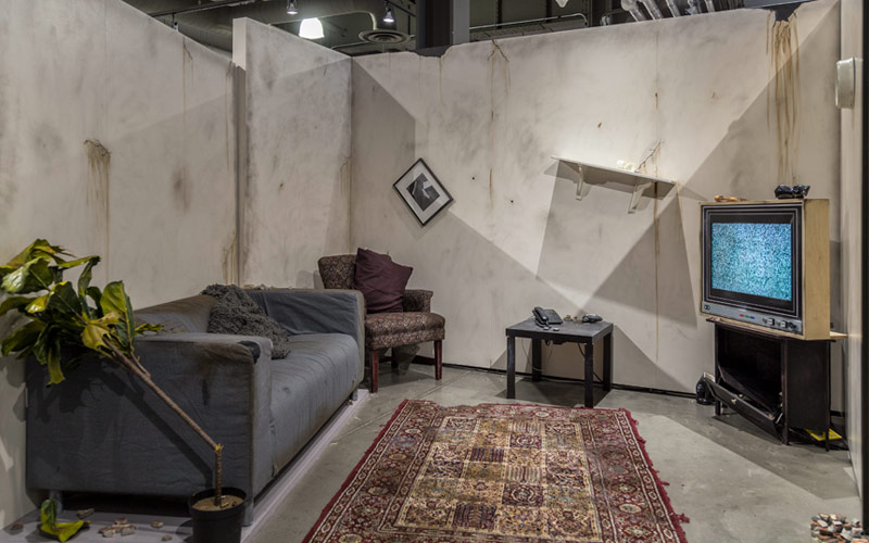 Exposition d’une pièce après sa destruction, avec les murs et les meubles endommagés.