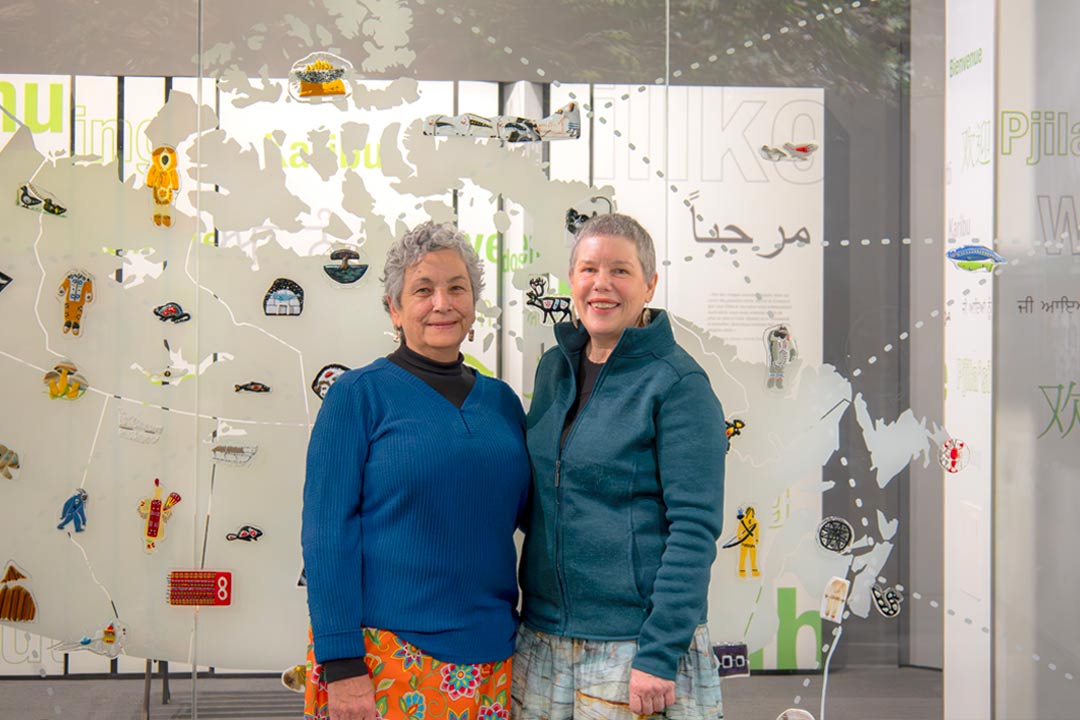 Deux femmes autochtones sourient devant leur installation d’art en verre.
