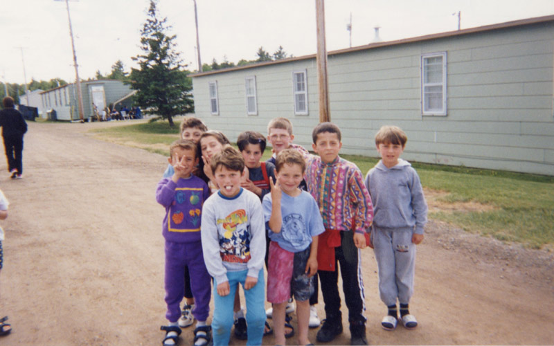 Un groupe d’enfants réfugiés kosovars pose sur un chemin de terre, plusieurs d’entre eux brandissant des signes de paix.