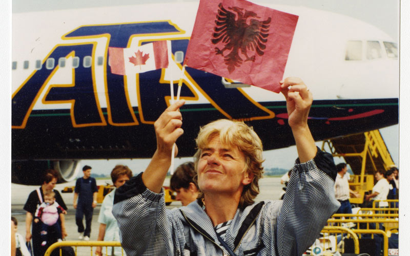 Un réfugié kosovar souriant et brandissant un petit drapeau albanais devant un avion.