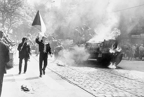 Des chars dans la rue et des gens qui marchent et tiennent un drapeau.