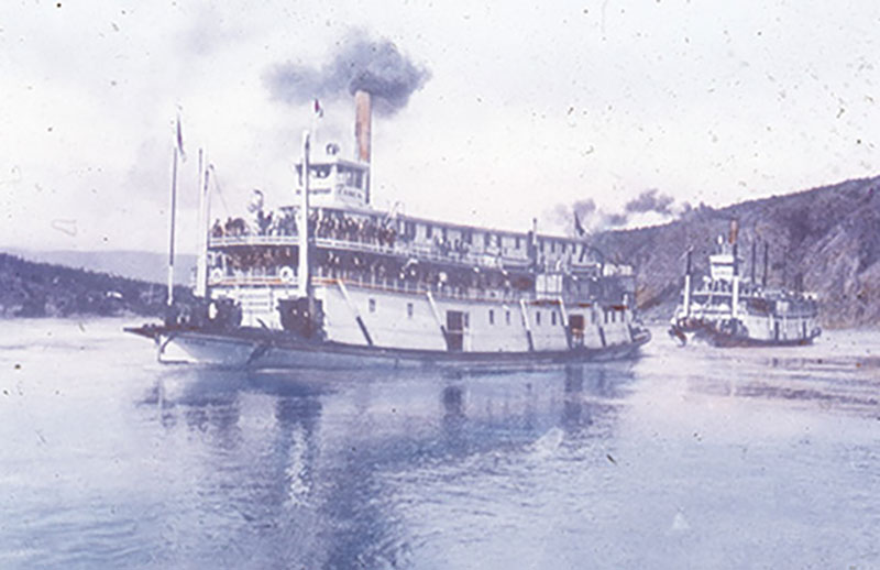 Deux bateaux à aubes avec des colonnes de fumée noire naviguent sur une rivière.