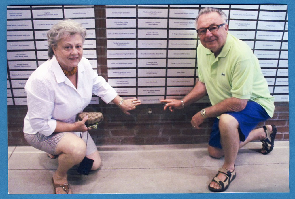 Un homme et une femme s'agenouillent devant un mur de plaques montées, ils pointent tous les deux vers l'une des plaques.