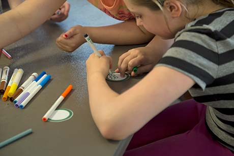 Une jeune fille dessine sur un petit cercle de papier à l’aide d’un feutre.