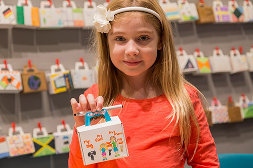 Une petite fille tient une valise en papier qu’elle a décorée.