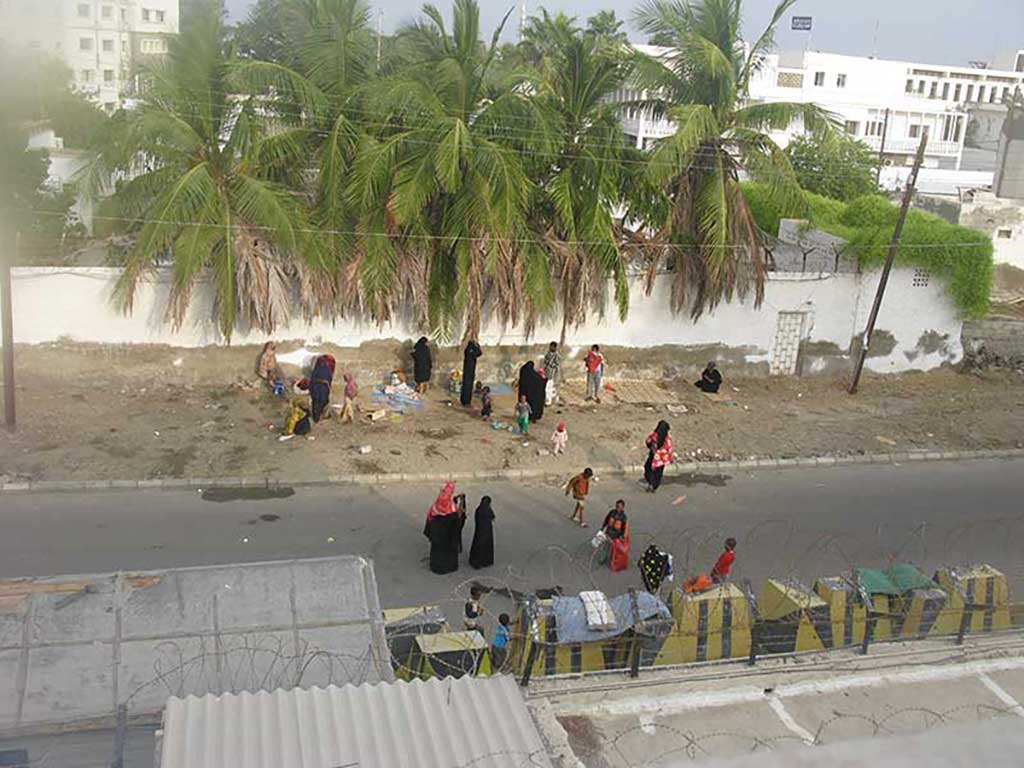 Une vue de la rue prise à partir d’un toit. Il y a des hommes, des femmes et des enfants assis sur des couvertures.