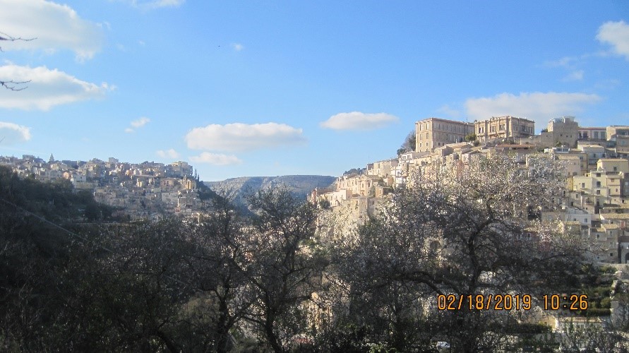 Une ville avec une vallée au milieu, vue de loin, avec des arbres devant et un ciel bleu en arrière-plan.