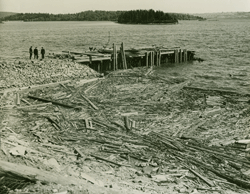 Vue aérienne de trois hommes à proximité d’un quai au bord de l’eau, des débris dans l’eau.