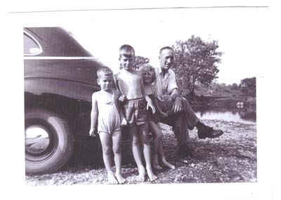 Le jeune George et trois enfants assis sur le pare-choc arrière d’une voiture.