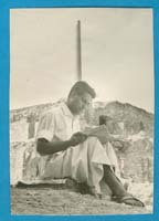 Jeune homme en robe blanche, assis et lisant.