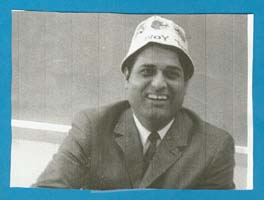 Homme en costume et cravate, avec un chapeau blanc.