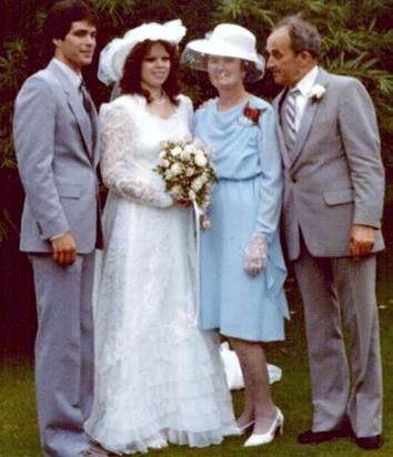Une scène de mariage avec la mariée et le marié debout sur une pelouse verte et un couple plus âgé se tiennent à côté d’eux.