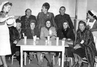 Plusieurs personnes assises et debout autour d’une table se faisant servir des boissons.