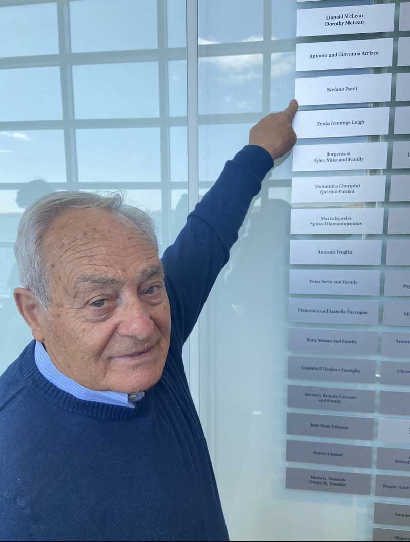 Un homme pointe une plaque sur un mur avec son nom dessus.
