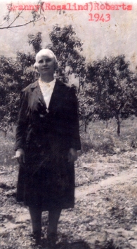 Femme debout dans un champ, des arbres derrière elle.