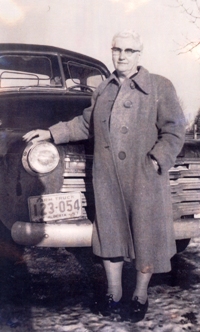 Femme portant des lunettes appuyée contre une vieille voiture.