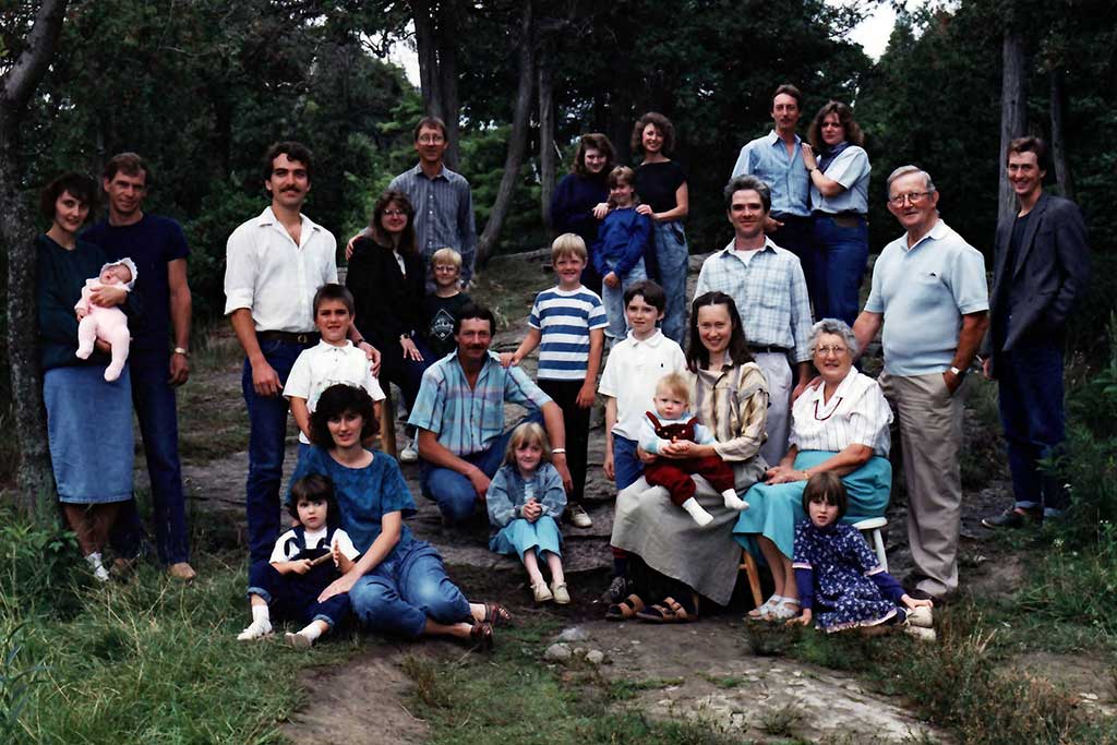 Un grand groupe de membres de la famille sont assis et debout à l’extérieur pour un portrait.